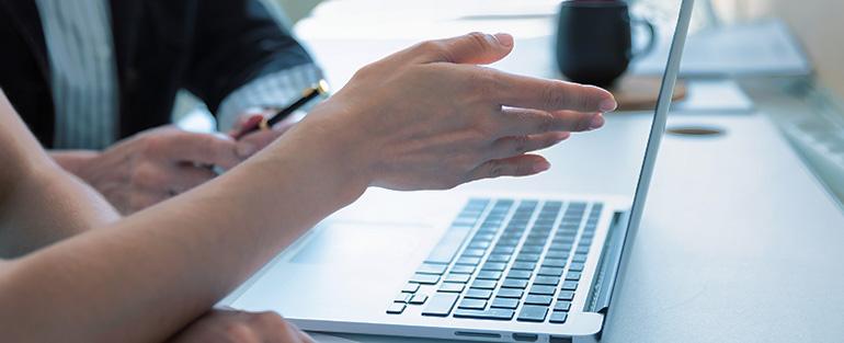 A person’s hand pointing an indication to a computer screen for another person